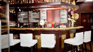 Una zona de bar con mostrador de madera, taburetes y una variedad de botellas y vasos.