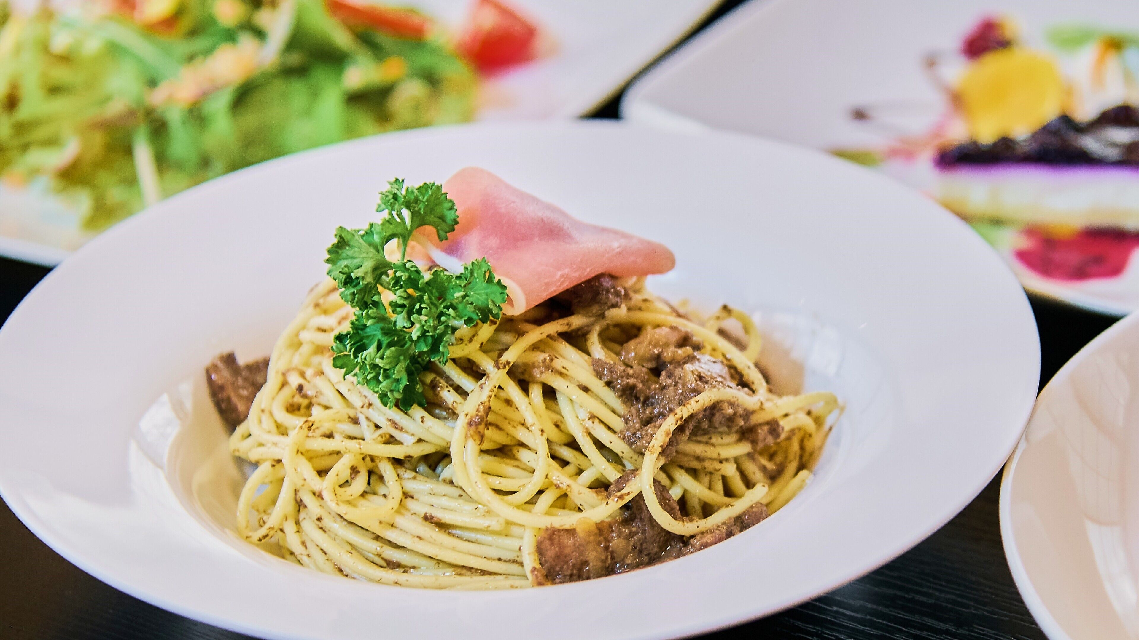 A plate of spaghetti with meat and a garnish of parsley and ham.
