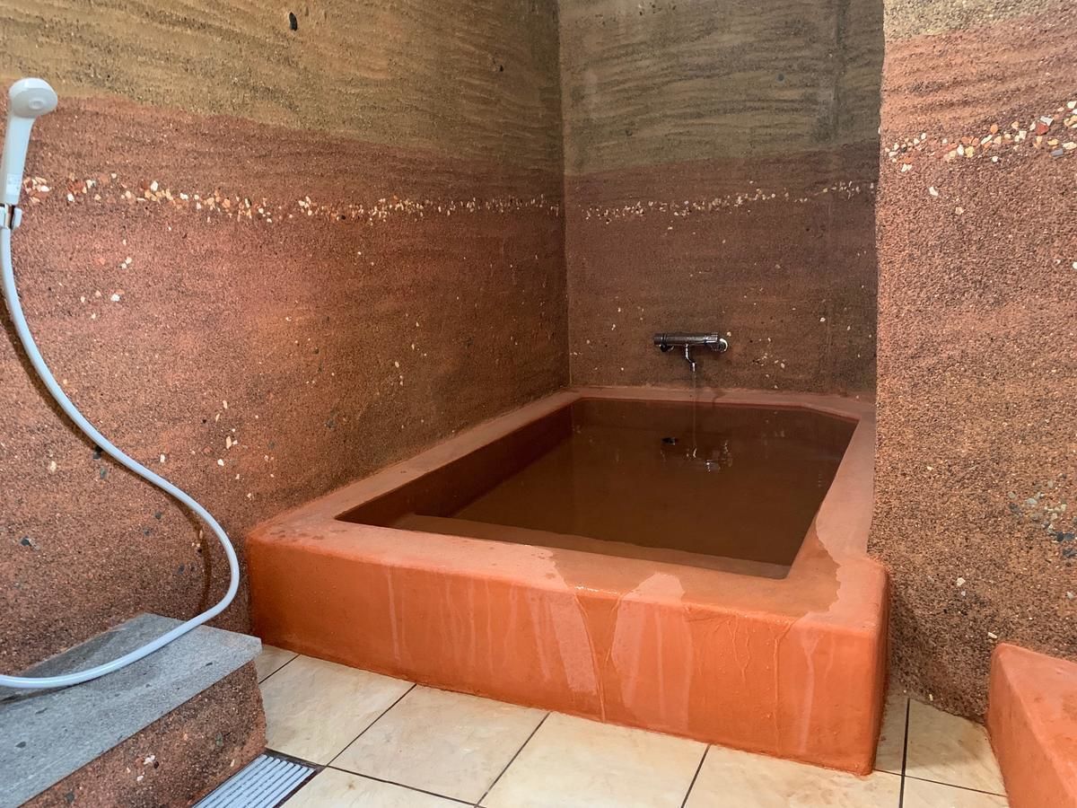 A rectangular hot tub with a metal faucet, surrounded by reddish-brown walls and a tiled floor.