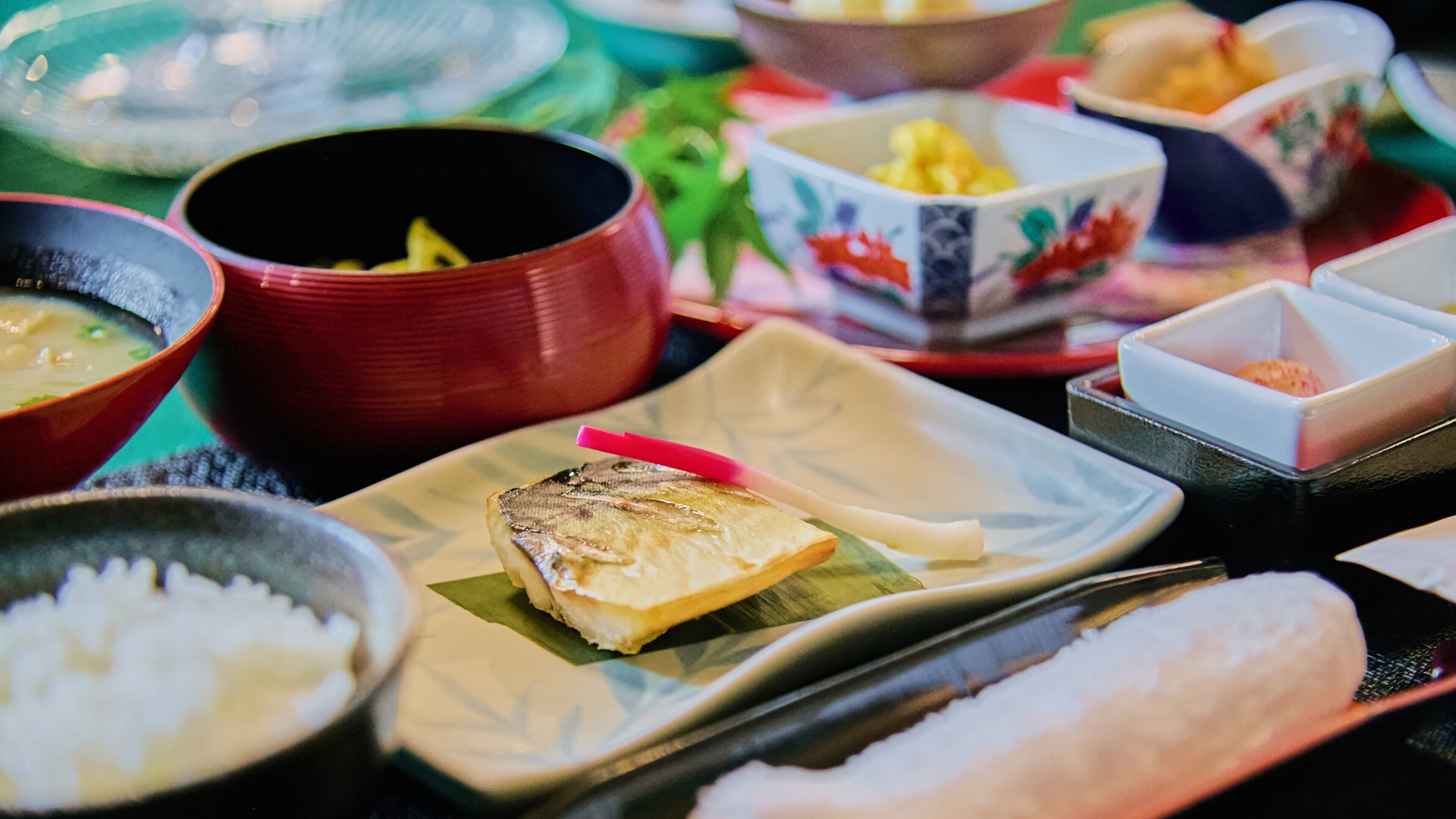 A variety of dishes on a table, including a fish on a leaf, bowls of soup, and other food items.