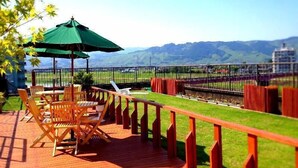 A wooden deck with outdoor furniture and a green umbrella, overlooking a fenced area with a view of distant hills. - Enmeikan (Asakura)