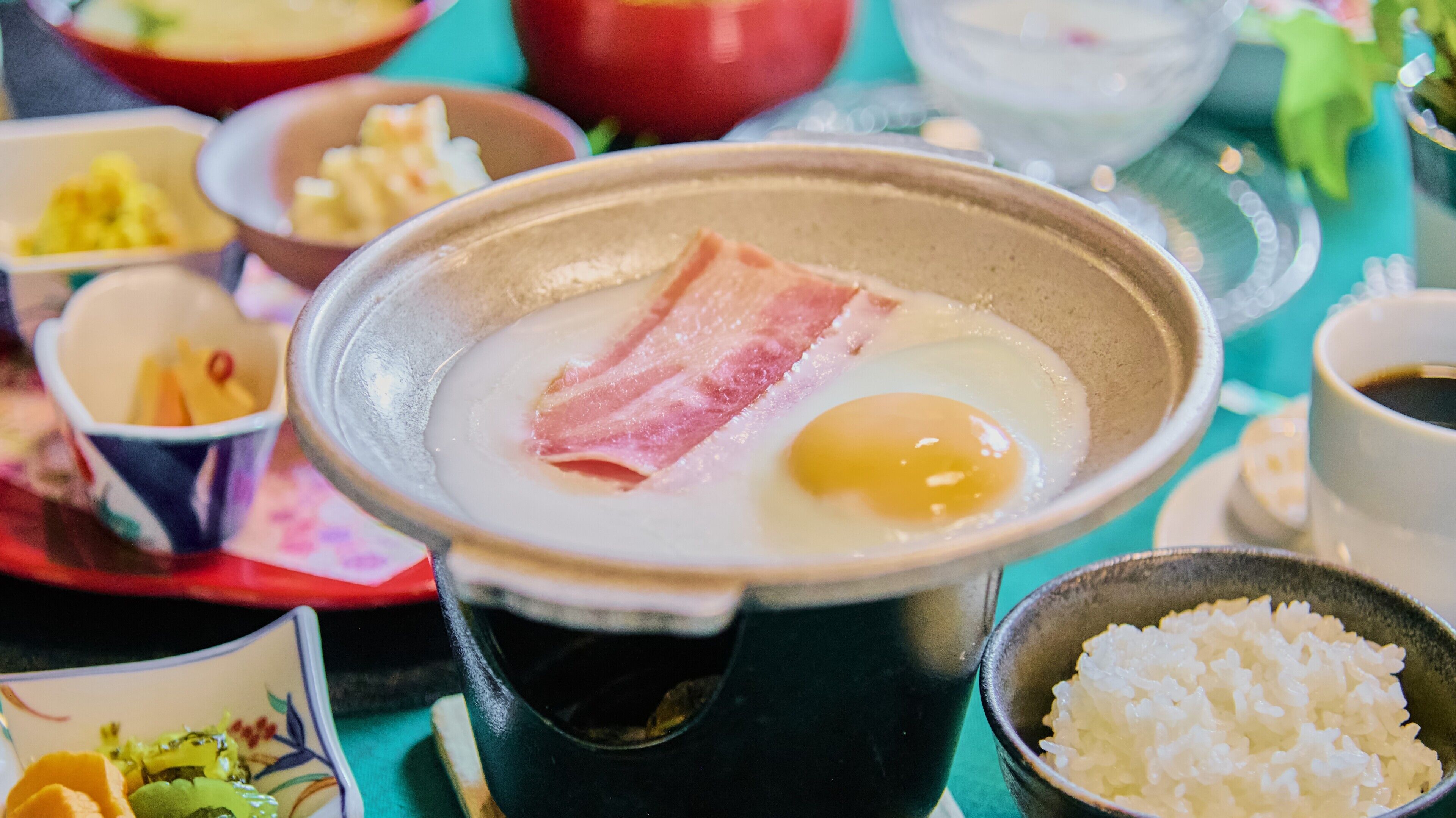 A hot pot with a piece of meat and an egg in the center, surrounded by various dishes and bowls.