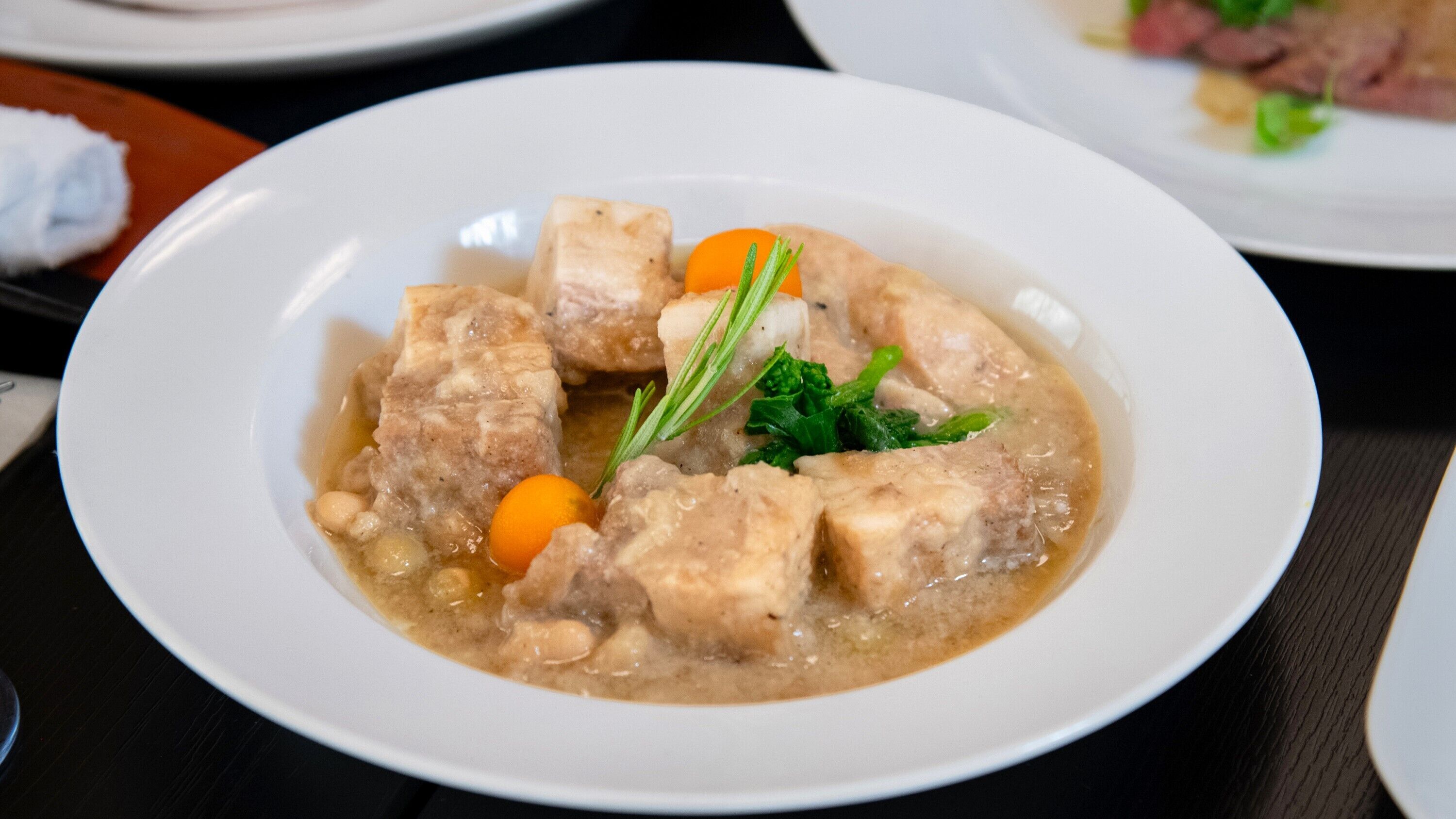 A white plate with a stew containing chunks of meat, carrots, and herbs.