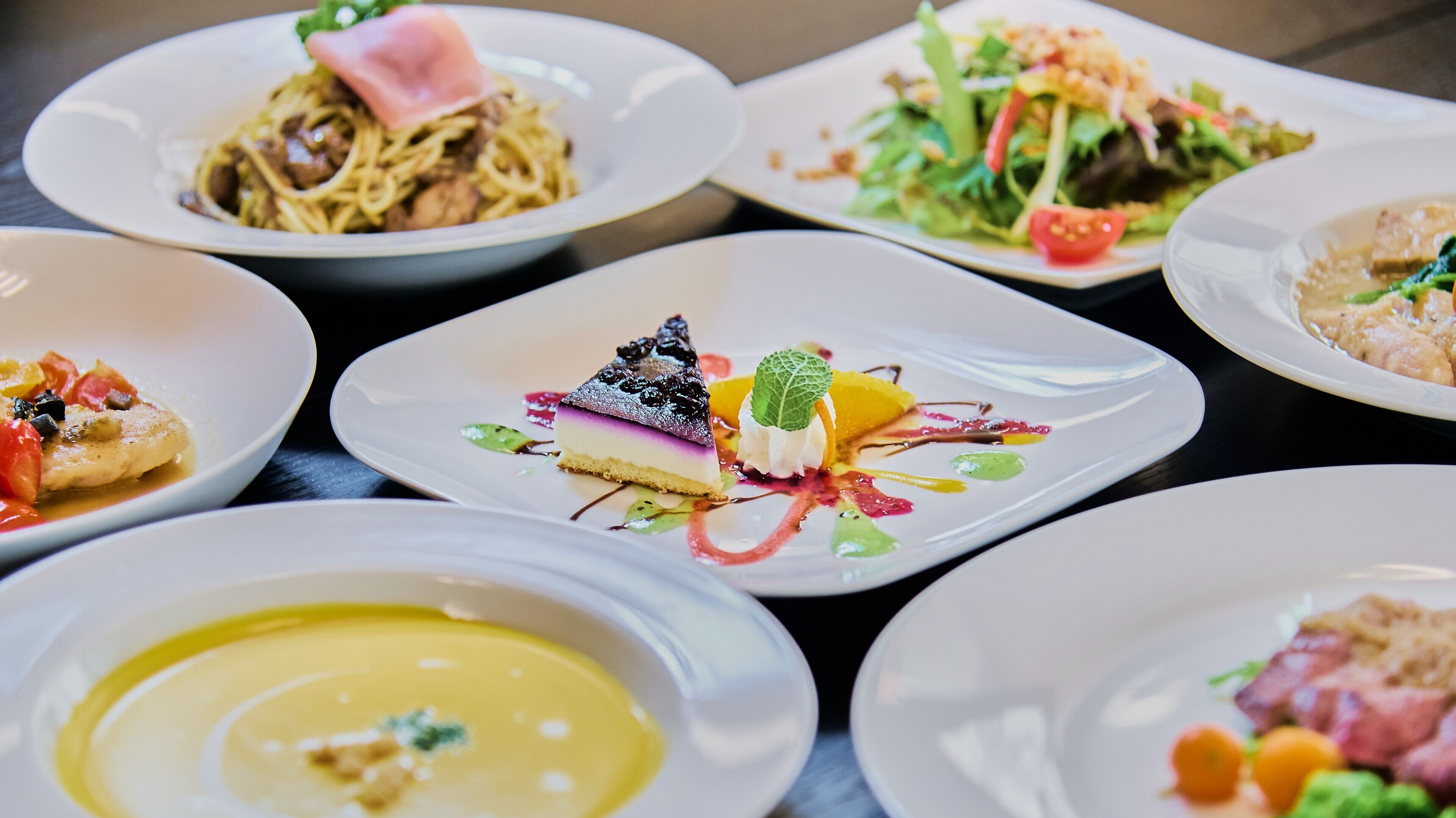 A variety of plated dishes, including a slice of cake with a berry topping and a salad with a tomato.