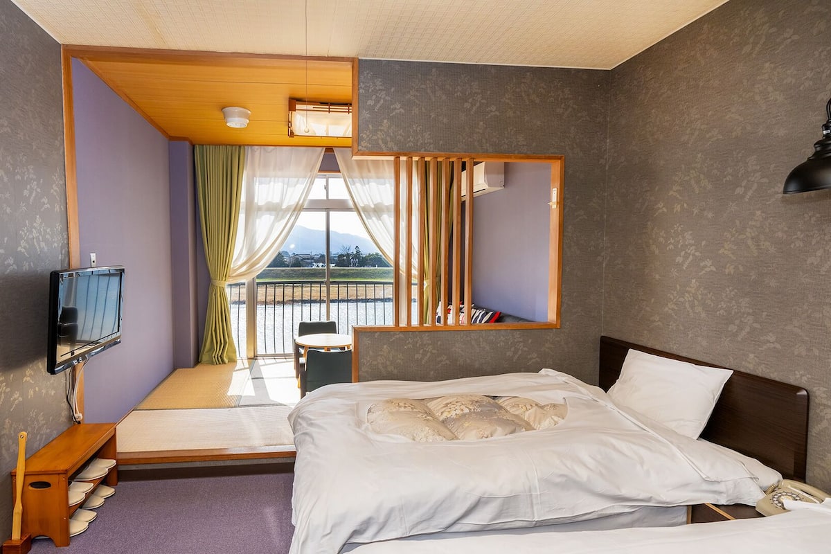 A compact hotel room with a bed, a TV, a small table, and a view of the outdoors.