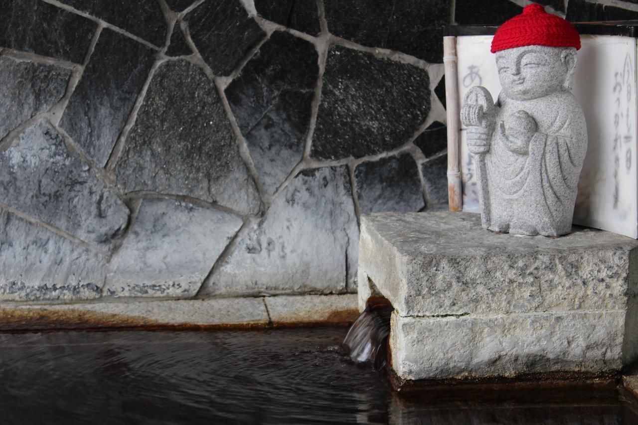 A stone statue of a figure with a red hat, placed on a stone platform next to a stone wall.