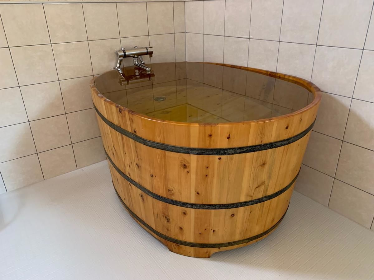 Una bañera de madera con cubierta de vidrio en un baño con paredes de azulejos.