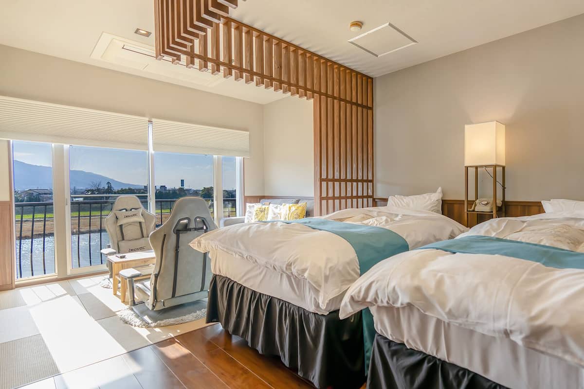 A hotel room with two beds, a chair, a lamp, and a view of a body of water.