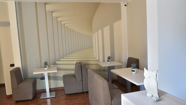 Un intérieur moderne avec un escalier central, des coins salon et une statue de hibou décorative.