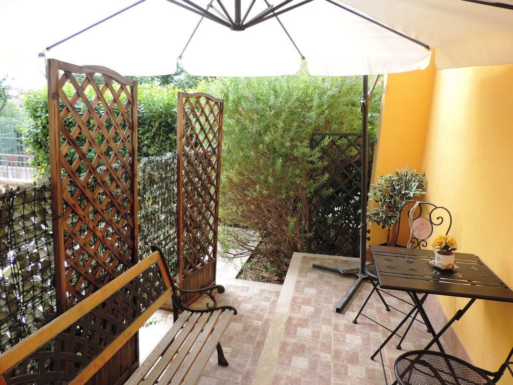 A patio area with a wooden bench, a metal table with chairs, and a white umbrella providing shade.