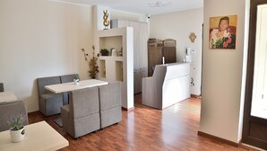 Un salon moderne avec un canapé gris, une petite table et un meuble blanc. Le sol est en bois et il y a un tableau accroché au mur.