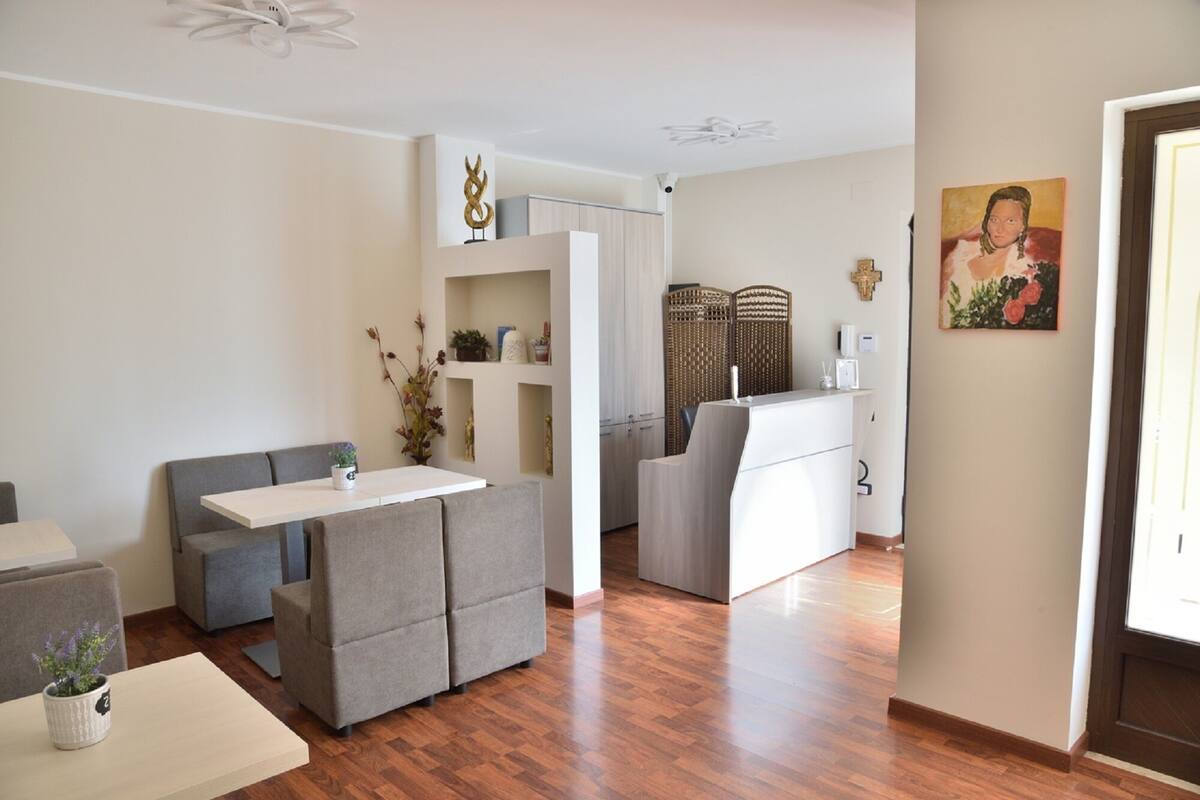 Ein modernes Wohnzimmer mit einem grauen Sofa, einem kleinen Tisch und einer weißen Kommode. Der Boden ist aus Holz und an der Wand hängt ein Gemälde.