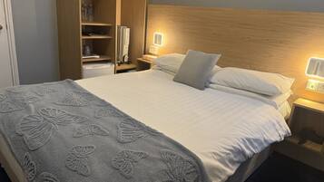 A neatly made bed with a grey blanket, a wooden headboard, bedside lamps, and a wardrobe with shelves.
