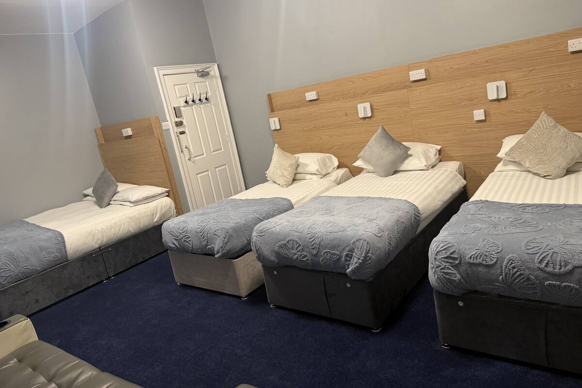 A hotel room with three beds, a wooden headboard, a door with a handle, and a blue carpet.
