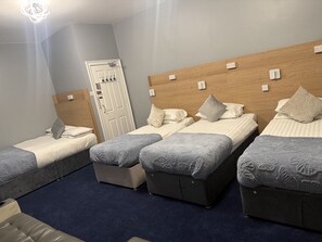 A hotel room with three beds, a wooden headboard, a door with a handle, and a blue carpet.