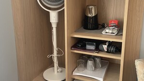 A wooden wardrobe with shelves holding towels, a kettle, a camera, and a small refrigerator. - Diamonds Inn Ltd (York)