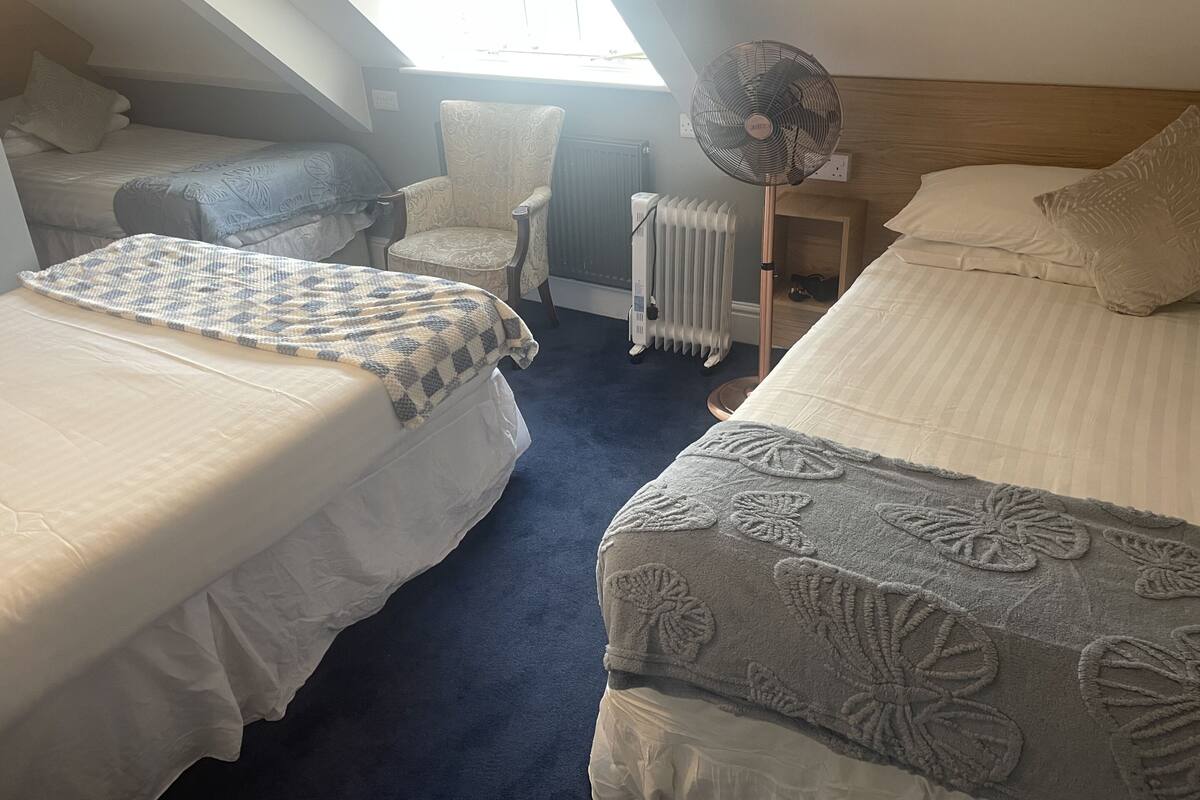 A room with two beds, a chair, a radiator, and a fan.