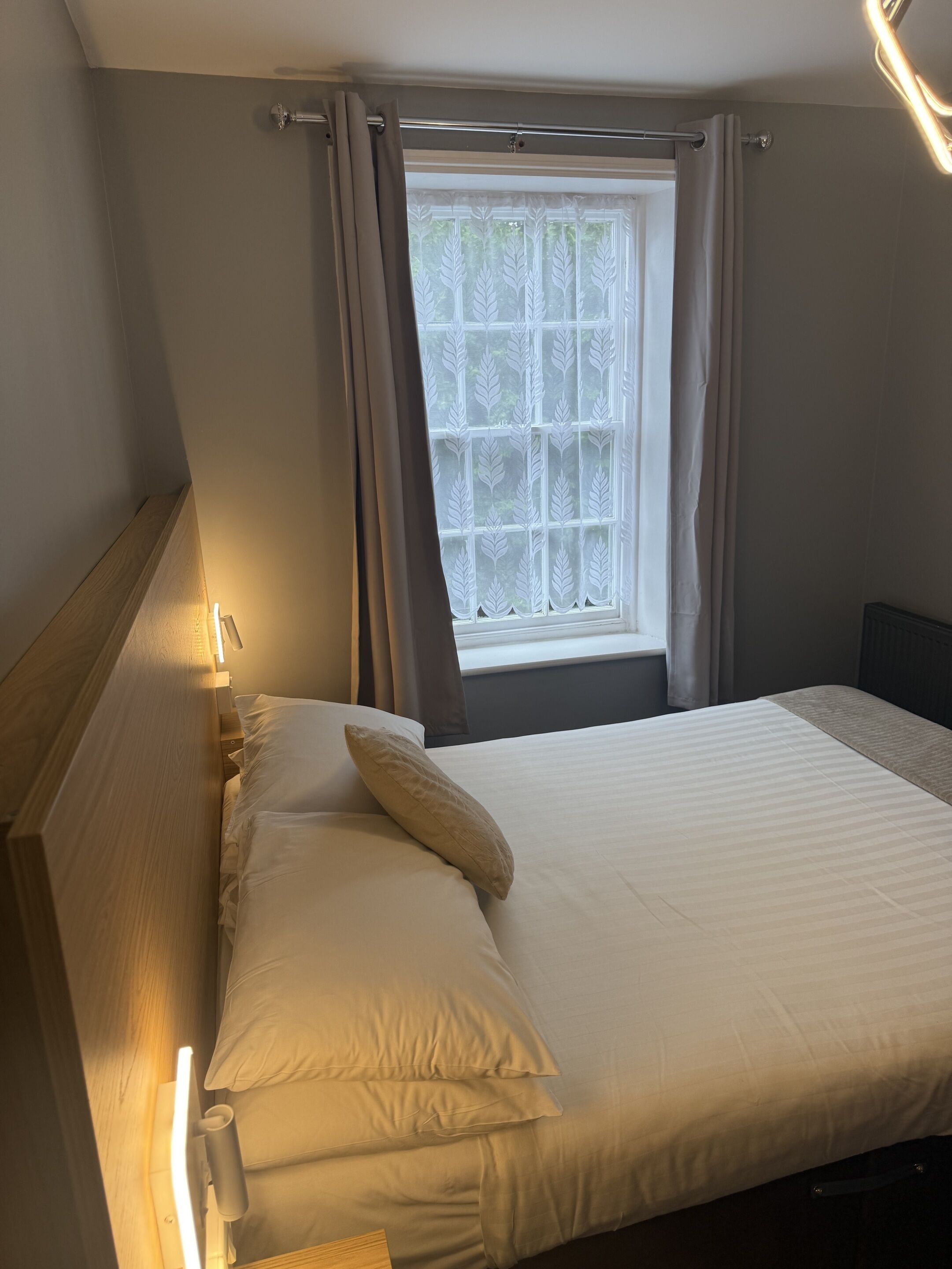 Een net opgemaakt bed met kussens, een houten hoofdbord en een raam met gordijnen.
