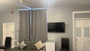 A room with a sofa, a television, a small refrigerator, and a door. - Diamonds Inn Ltd (York)