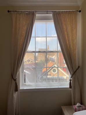 A room with a window featuring a view of buildings and a clear sky.