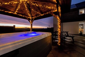 A hot tub under a wooden pergola with string lights, overlooking a sunset view. - Elderburn Luxury Lodges (St. Andrews)