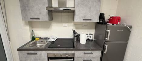 A compact kitchen with grey cabinets, a built-in oven, a sink, and a refrigerator.