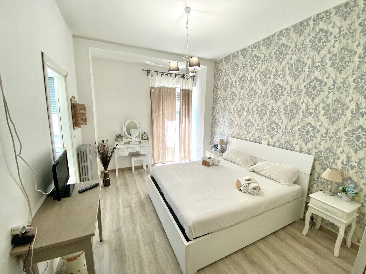 Un dormitorio con una cama grande, un escritorio, una silla, un espejo y una mesita de noche con lámpara.