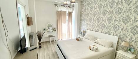 Un dormitorio con una cama grande, un escritorio, una silla, un espejo y una mesita de noche con lámpara.