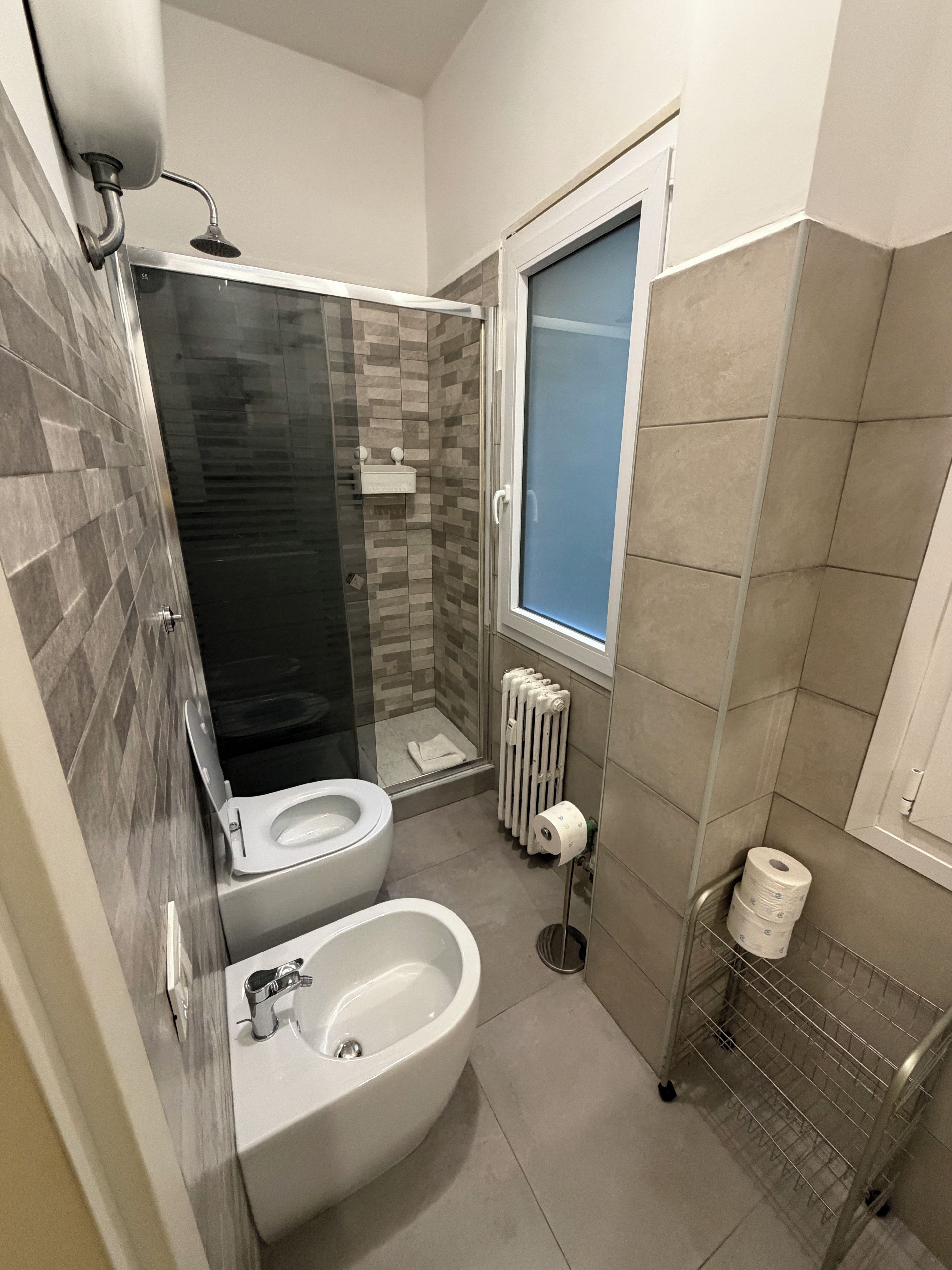 A modern bathroom with a shower, toilet, bidet, and a toilet paper holder.