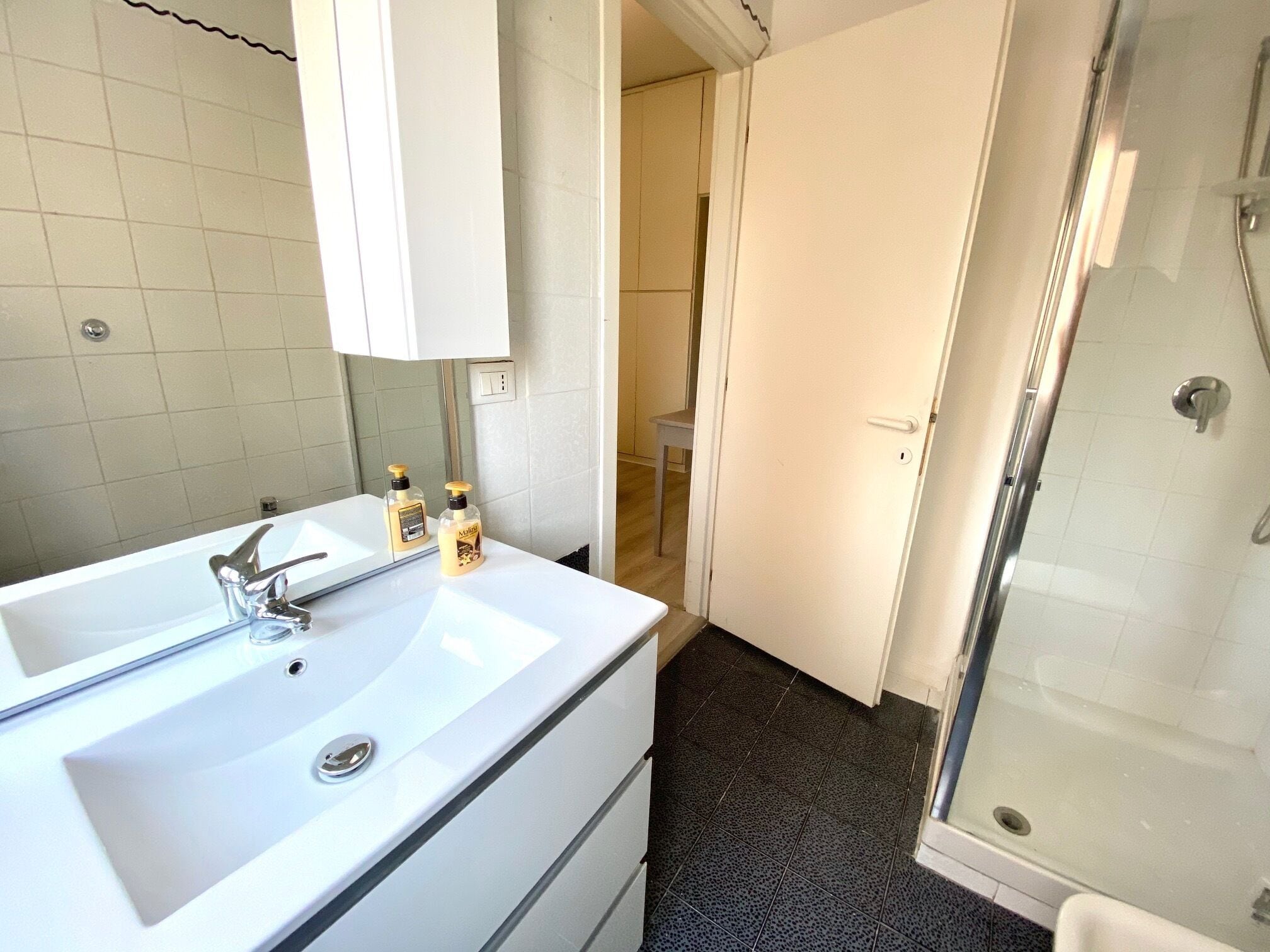 A bathroom with a white sink, mirror, and shower. There are two bottles of lotion on the sink.