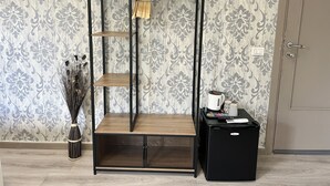 A room with a black metal shelving unit, a small black refrigerator, and a vase with dried plants. - A Quattro Passi Da (Rome)