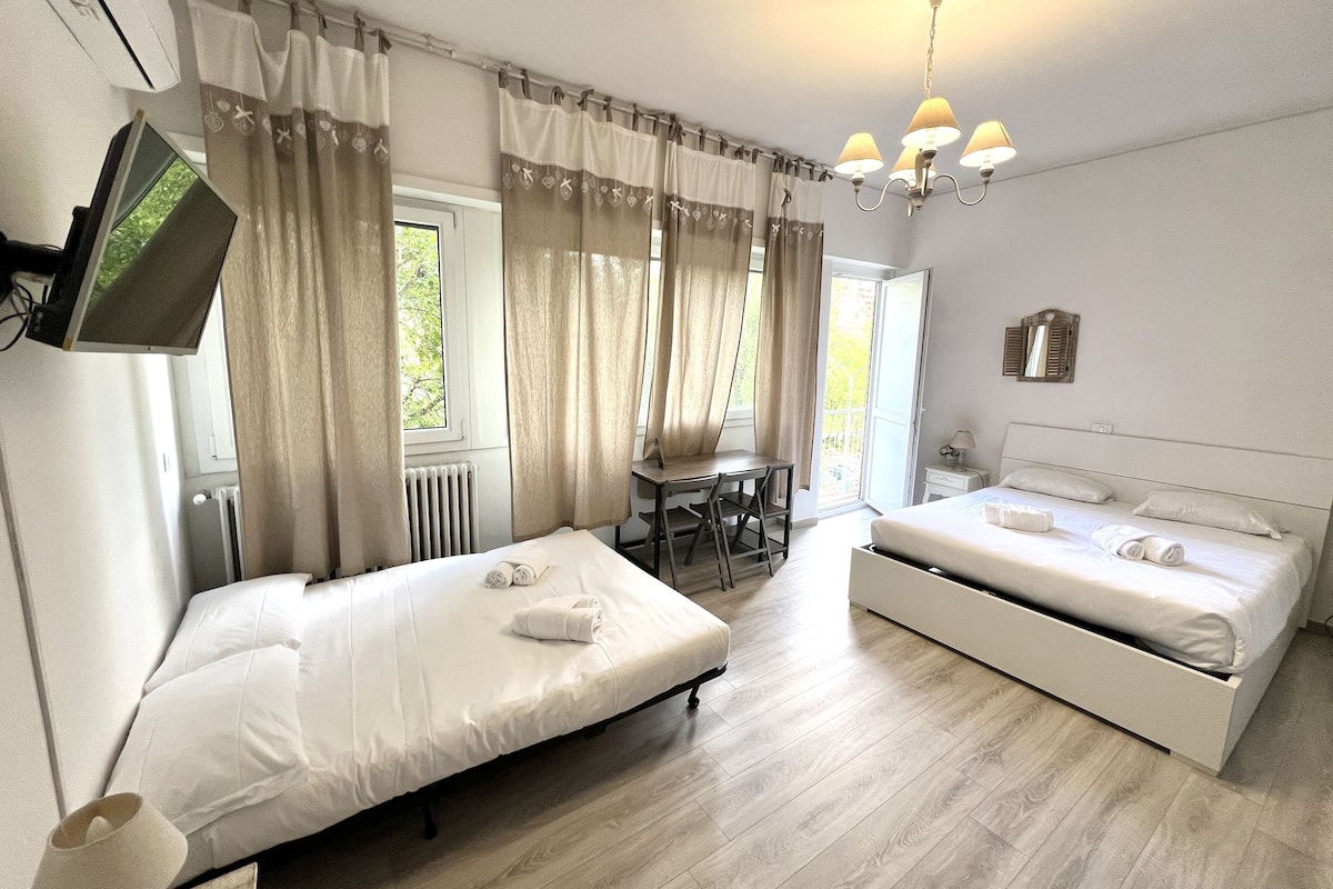 A hotel room with two beds, a desk, a chair, a TV, and a balcony with curtains.