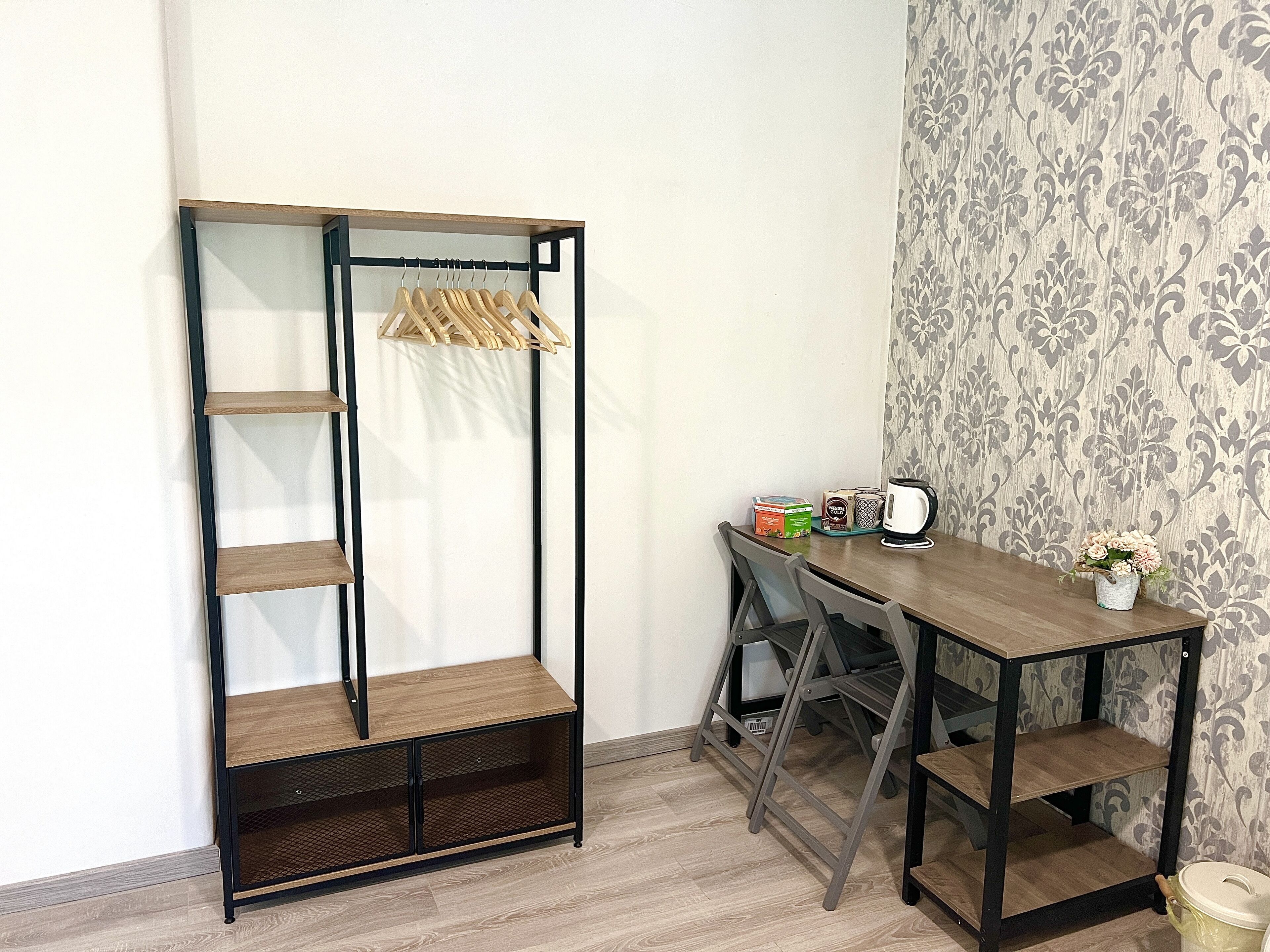 A corner room with a wooden wardrobe, a small table with a kettle, and a potted plant.