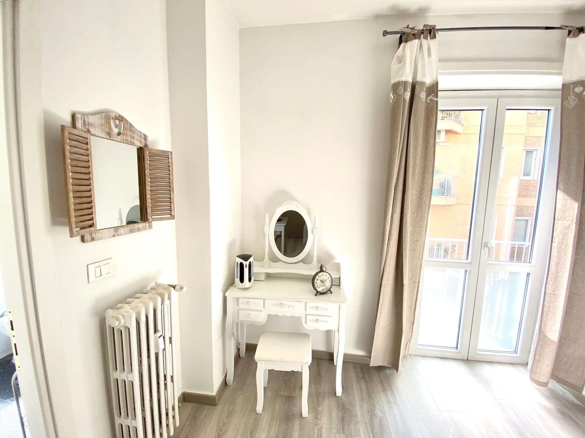 Une chambre avec une commode blanche, un miroir, une horloge et un radiateur.