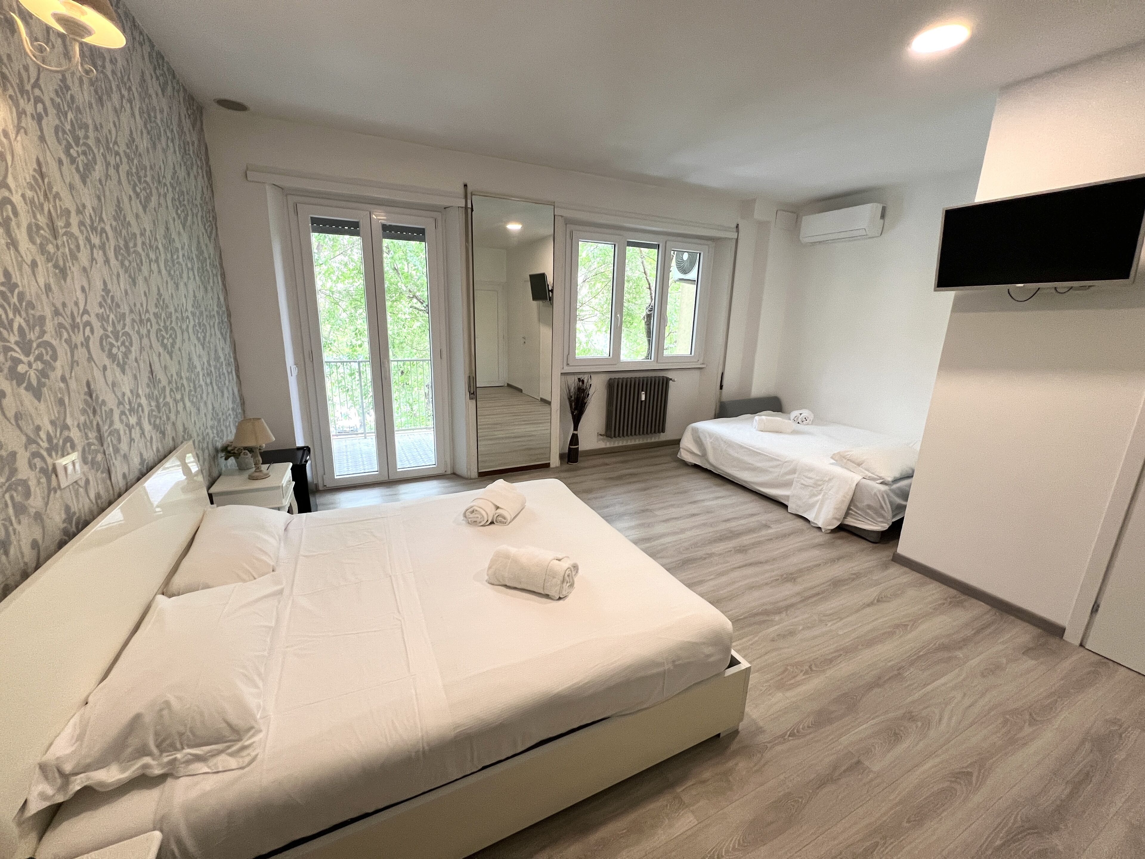 Ein Hotelzimmer mit einem großen Bett, einem kleineren Bett, einem Fernseher und Blick auf Grün hinter den Fenstern.