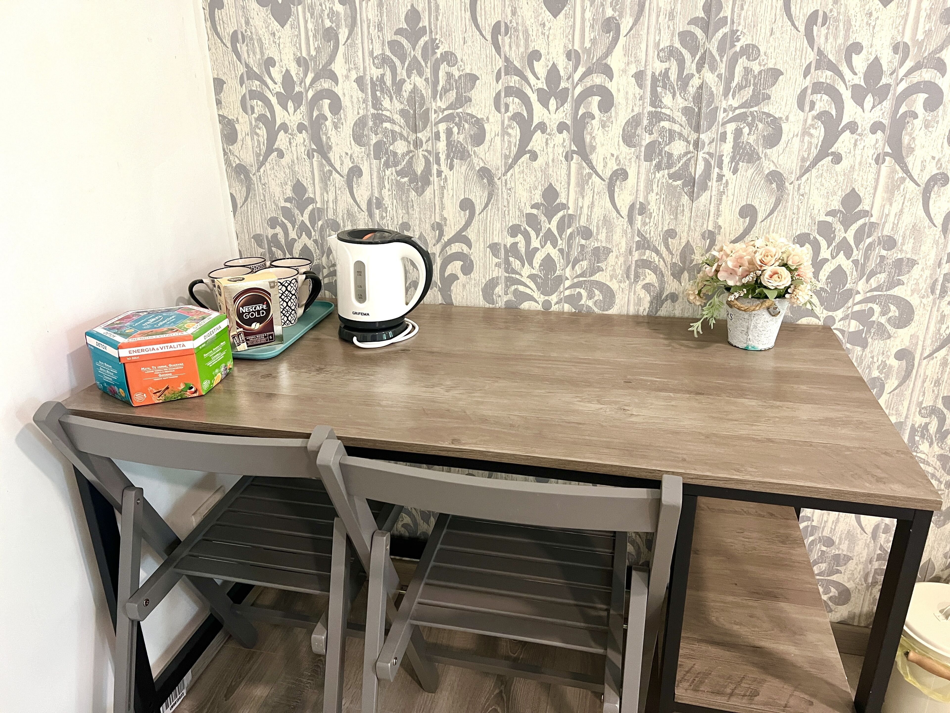 A wooden table with a coffee maker, a box of Nescafé Gold, and a potted plant.