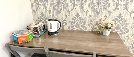 A wooden table with a coffee maker, a box of Nescafé Gold, and a potted plant.
