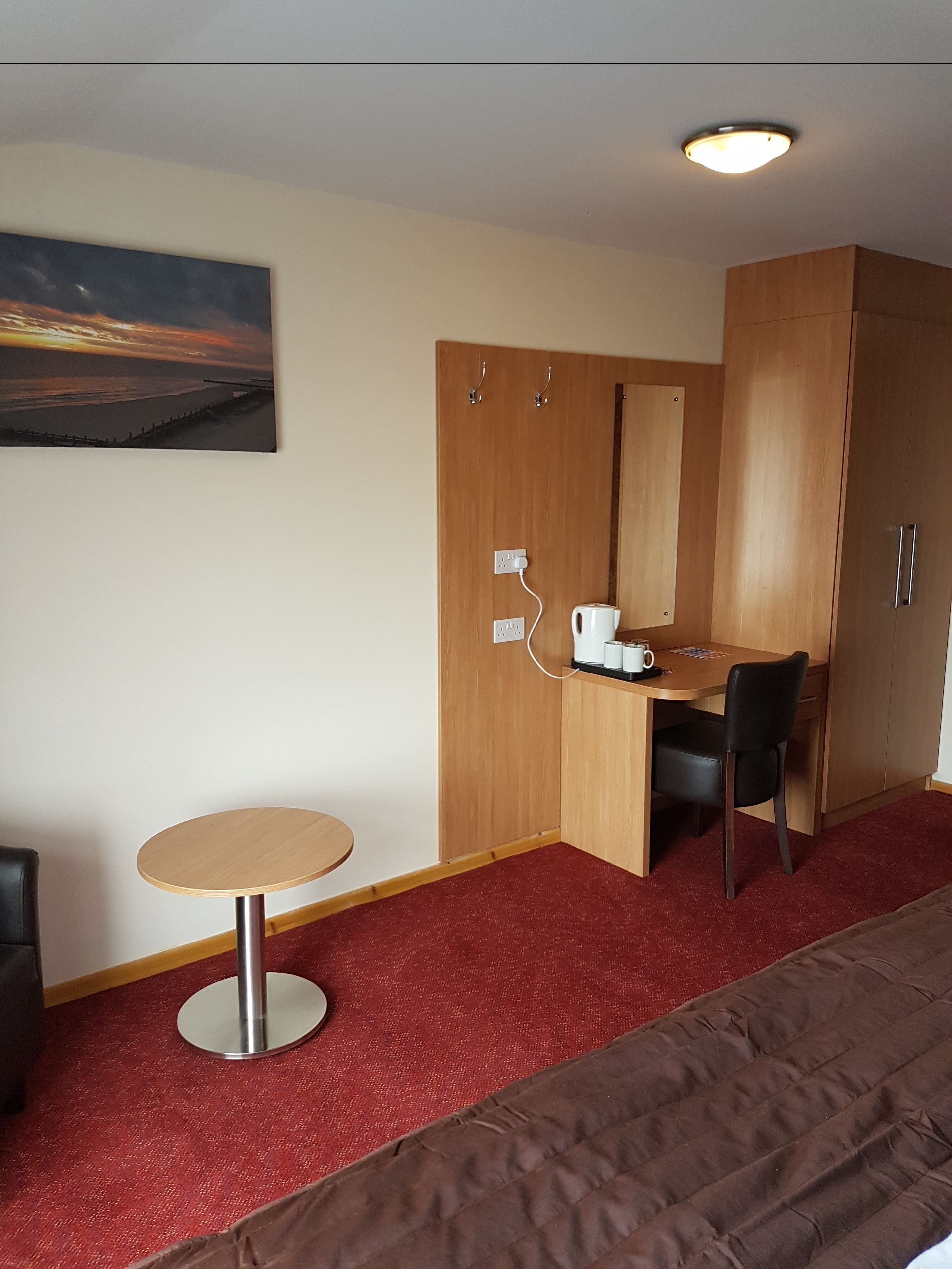 A hotel room with a bed, a desk with a chair, a small round table, and a painting on the wall.
