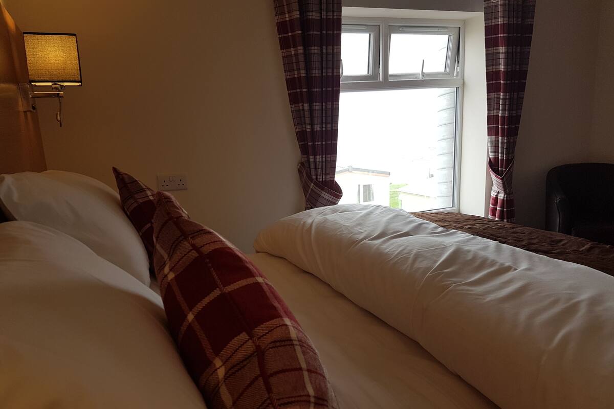 A hotel room with two beds, a lamp, a window with curtains, and a chair.