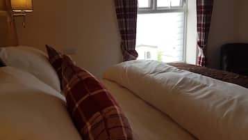 Une chambre d’hôtel avec deux lits, une lampe, une fenêtre avec des rideaux et une chaise.