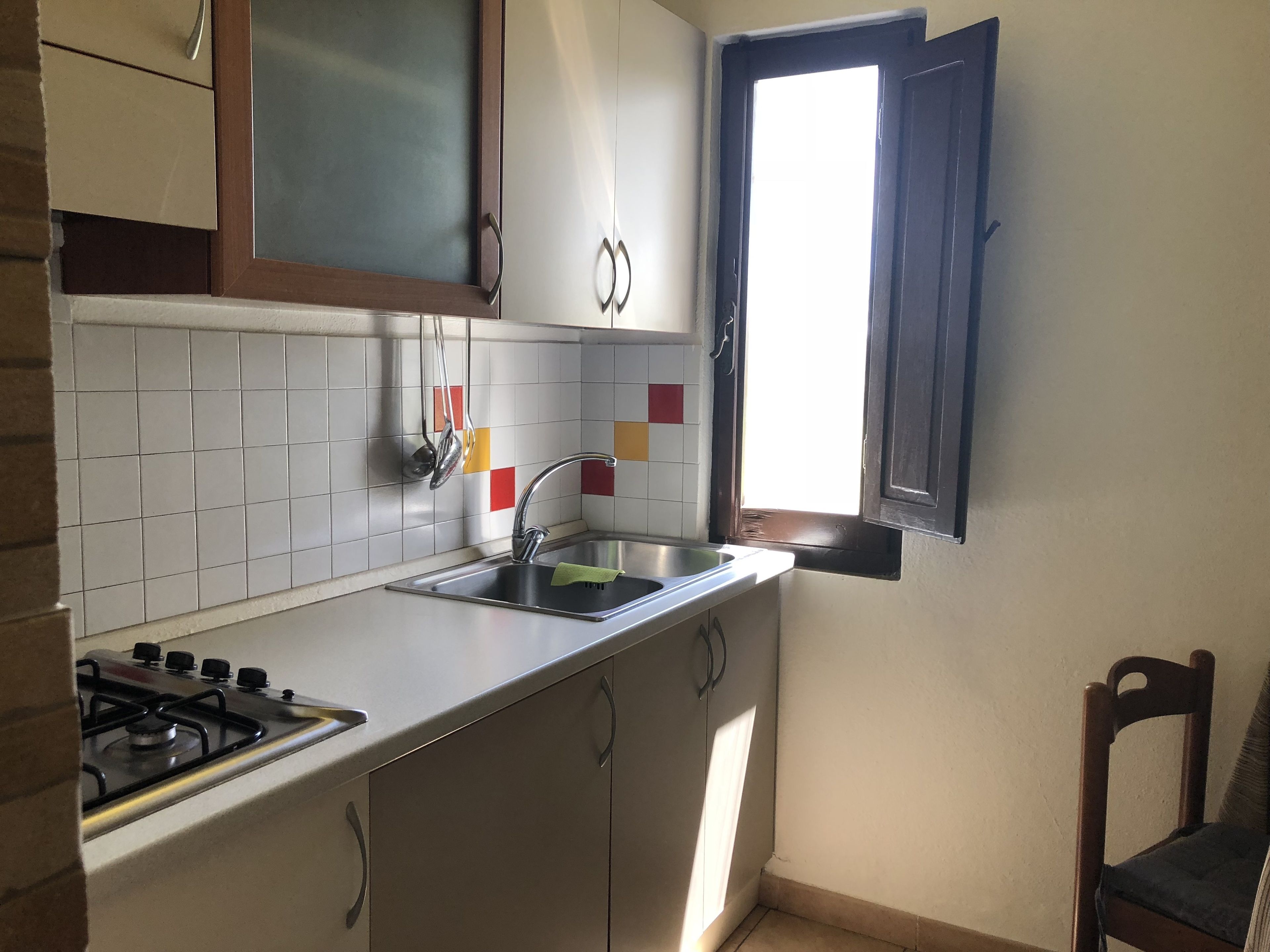 A kitchen with a gas stove, a sink, cabinets, and a window with a view.