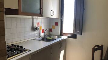 A kitchen with a gas stove, a sink, cabinets, and a window with a view.