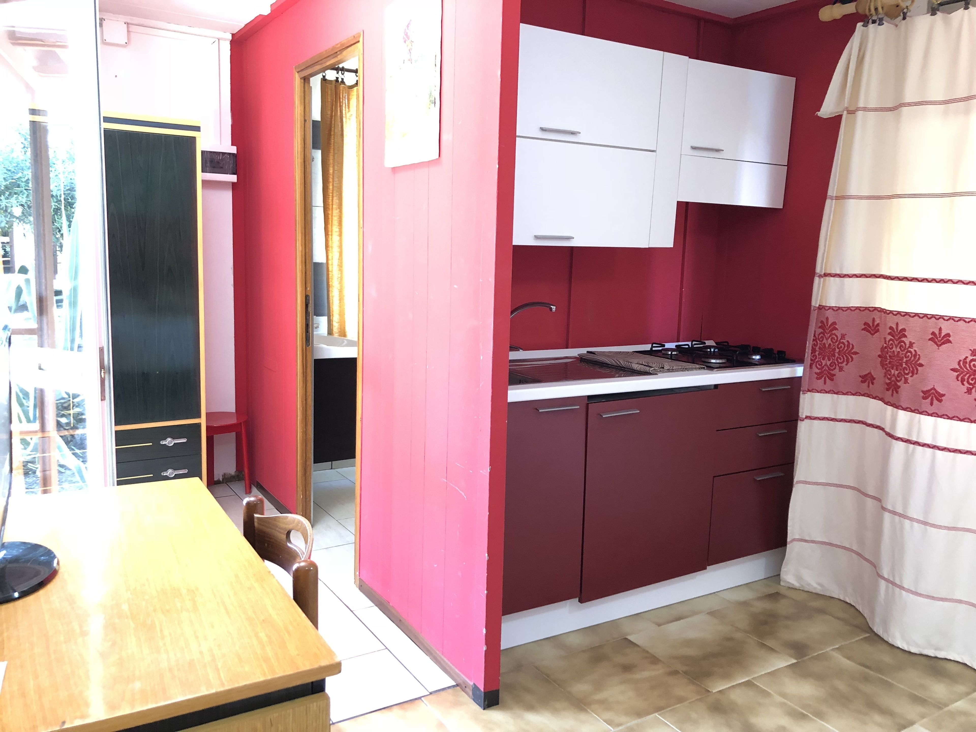 Une cuisine de taille réduite avec des murs rouges, des placards blancs et une table à manger en bois.