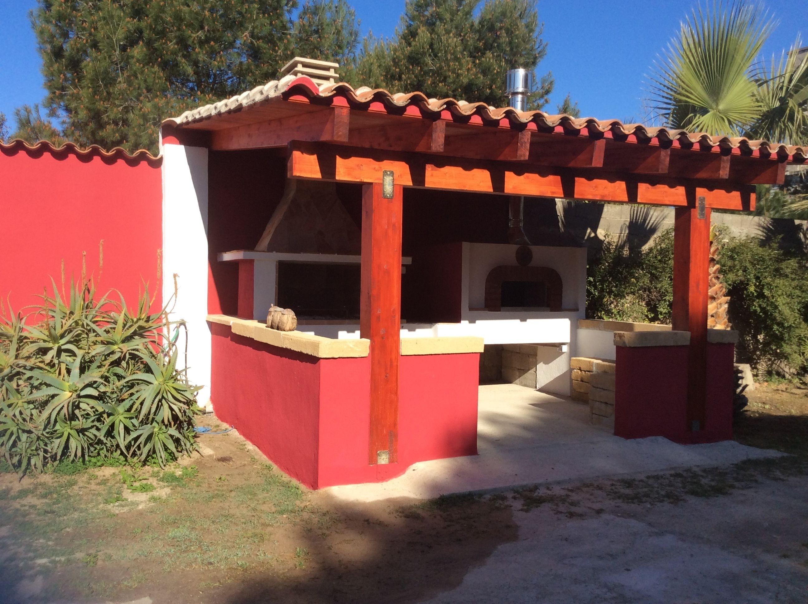 A red outdoor barbecue area with a chimney, a wooden table, and a bench.