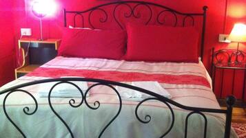 A bed with a metal frame, red walls, and a single artwork above it.