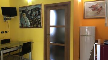 Una cocina funcional con una mesa de vidrio, sillas, un refrigerador y dos cuadros en las paredes.