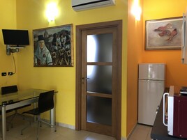 Una cocina funcional con una mesa de vidrio, sillas, un refrigerador y dos cuadros en las paredes.