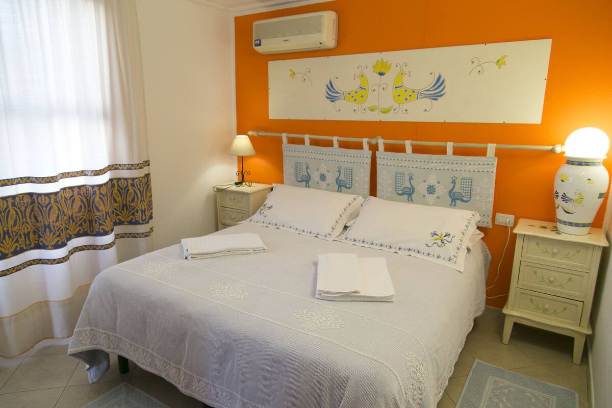 Un dormitorio con una cama, mesitas de noche, una lámpara, un florero y un adorno en la pared.