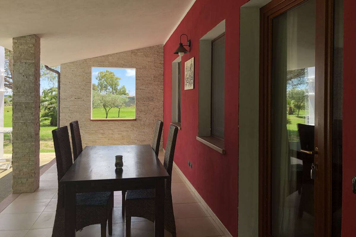 Un comedor con mesa y sillas, una ventana con vistas a árboles y una pared roja.