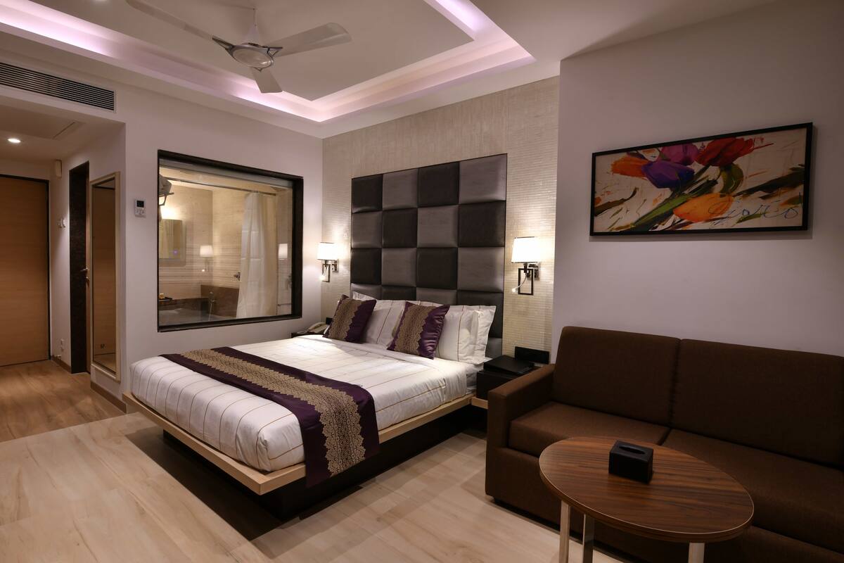 Una habitación de hotel moderna con una cama grande, un sofá, una pequeña mesa y un cuadro en la pared.